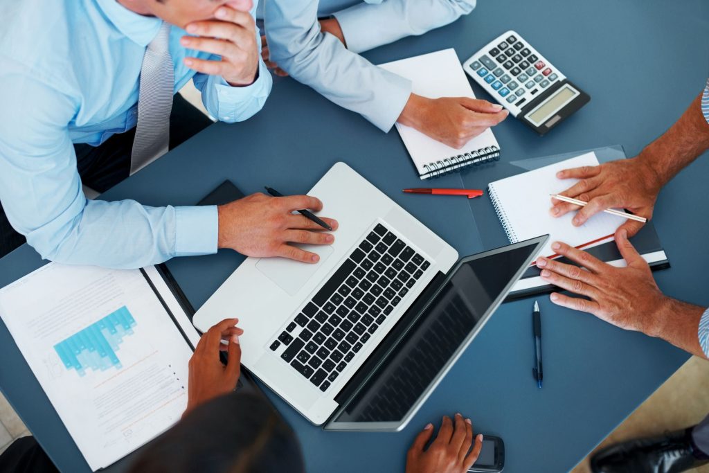 A group of people sitting around a table with laptops.